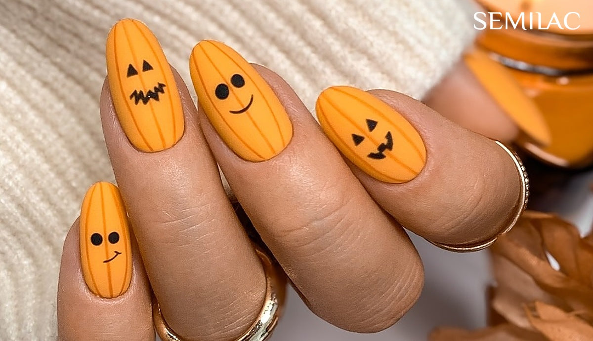 Matte orange gel nails with jack-o-lantern faces painted in black, held against a cream knit jumper