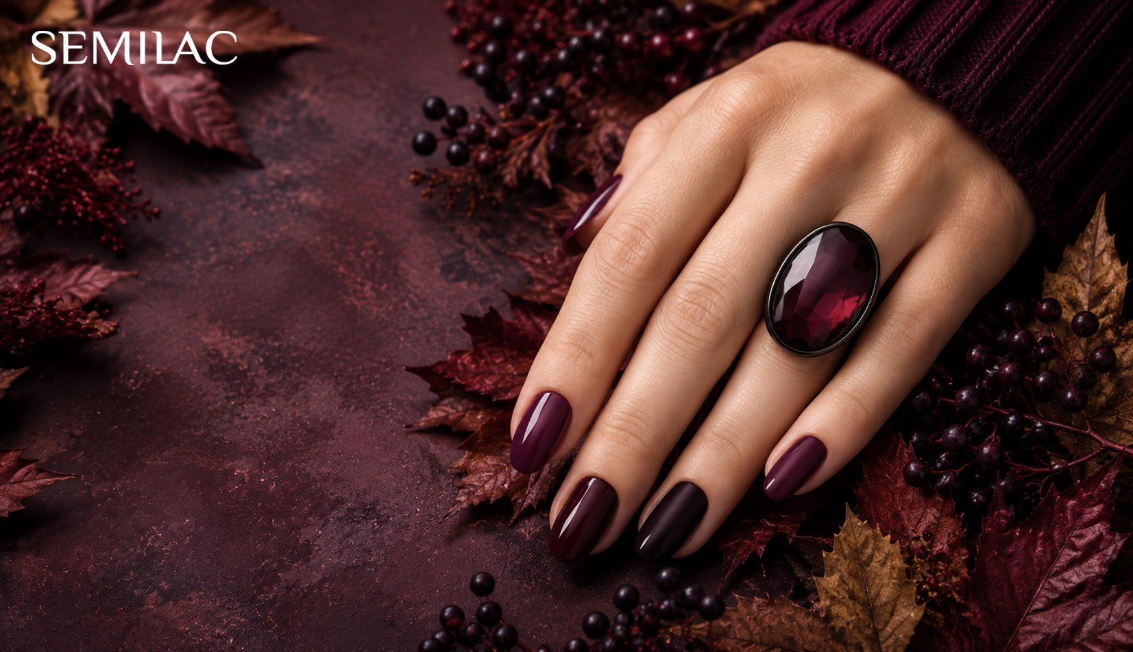 Hand wearing deep plum and burgundy gel nails resting on autumn leaves and dark berries