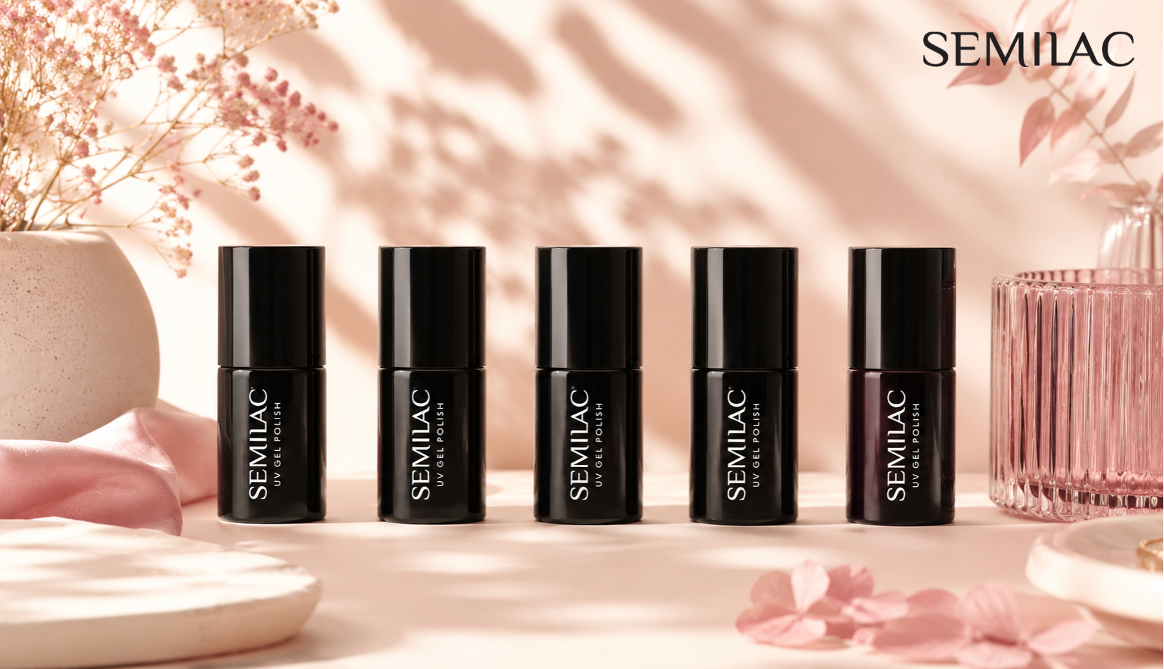 Five Semilac gel polish bottles lined up in a row on a pale pink surface beside dried flowers