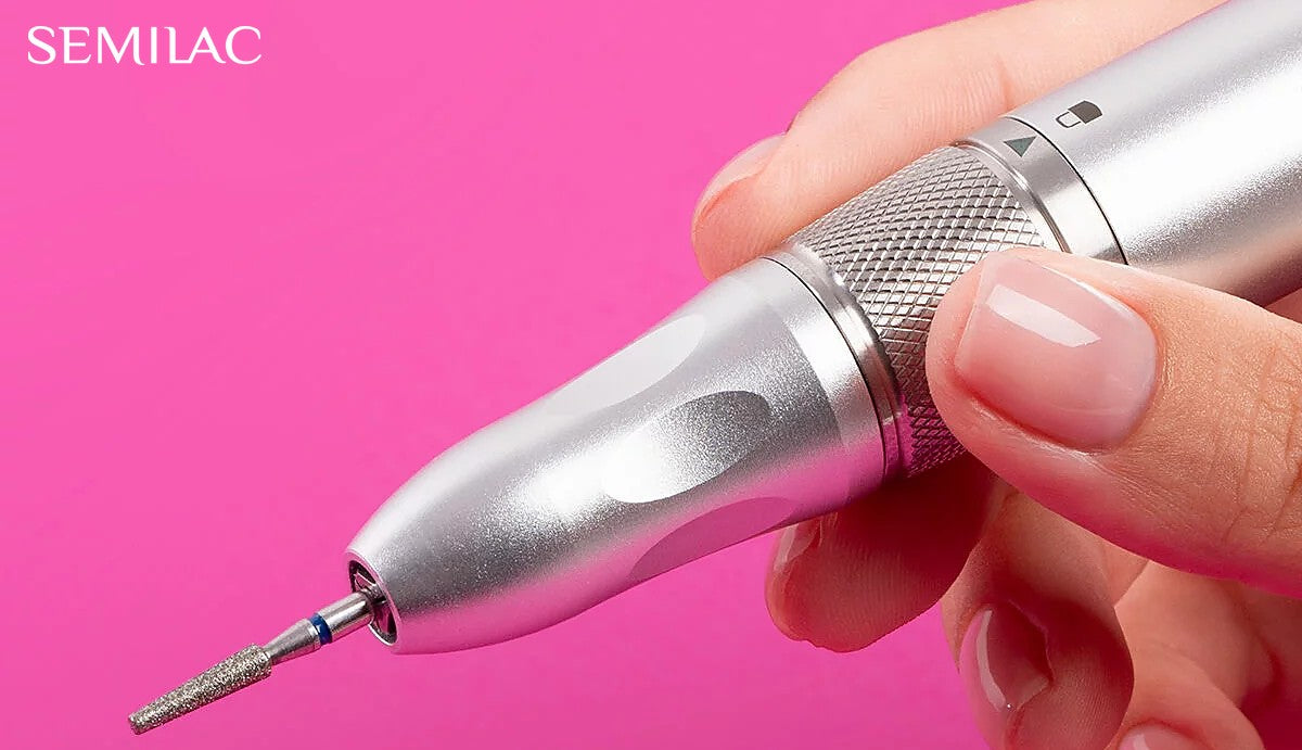 Silver nail drill handpiece with a diamond bit held against a pink background